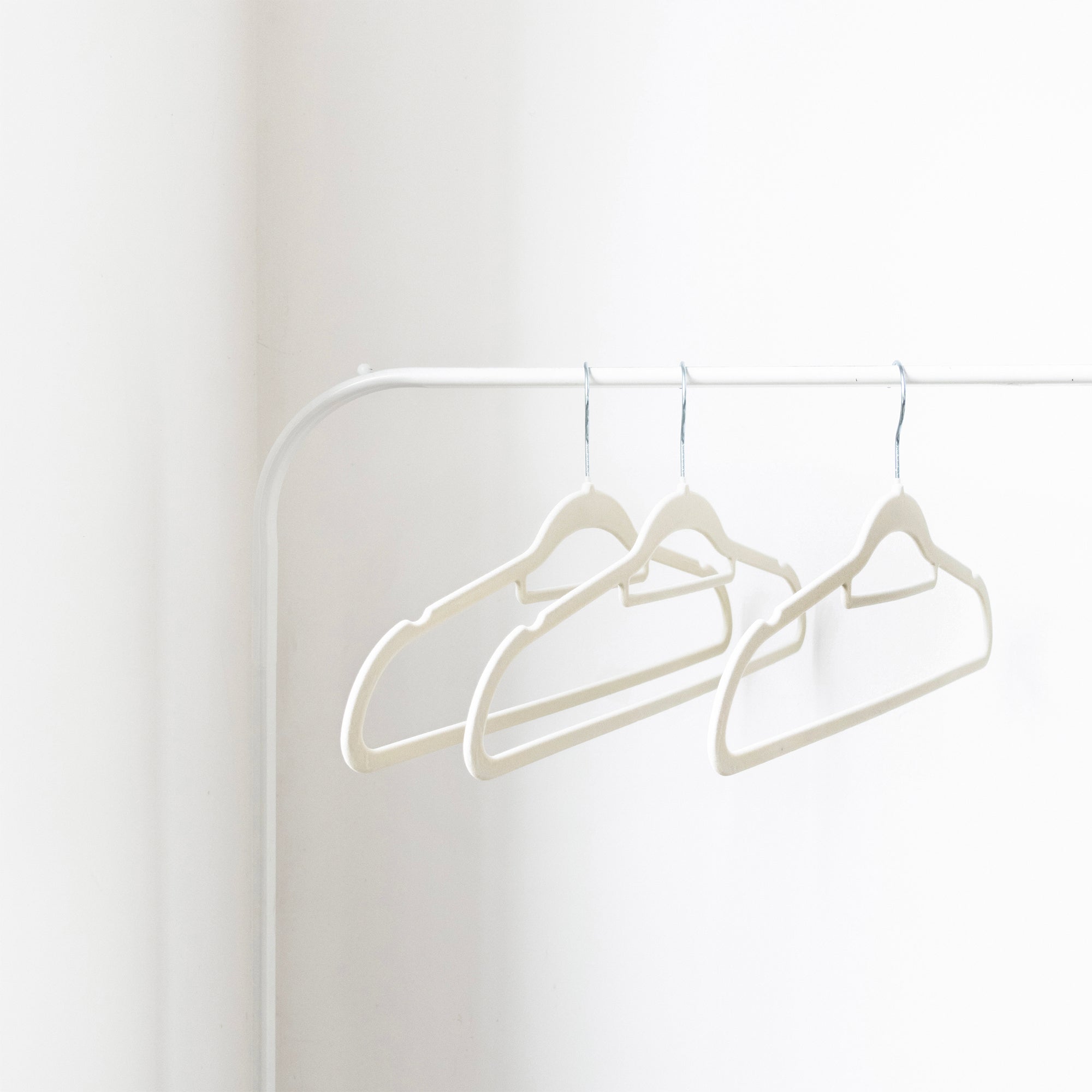 Three white hangers on a white rod against a white wall
