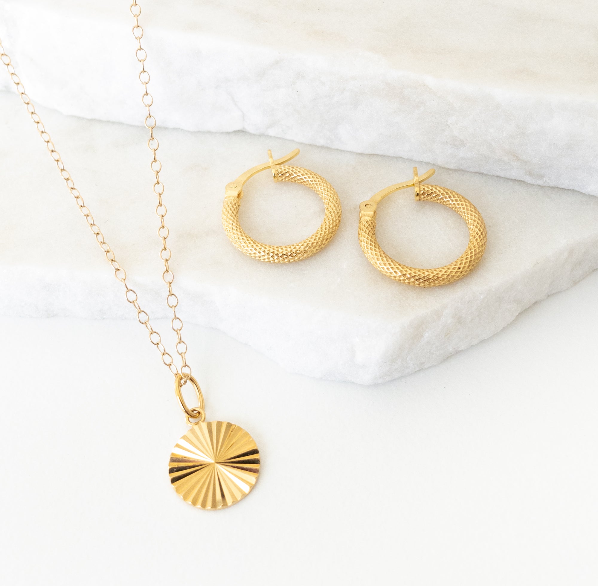 Gold necklace and hoop earrings on a marble surface
