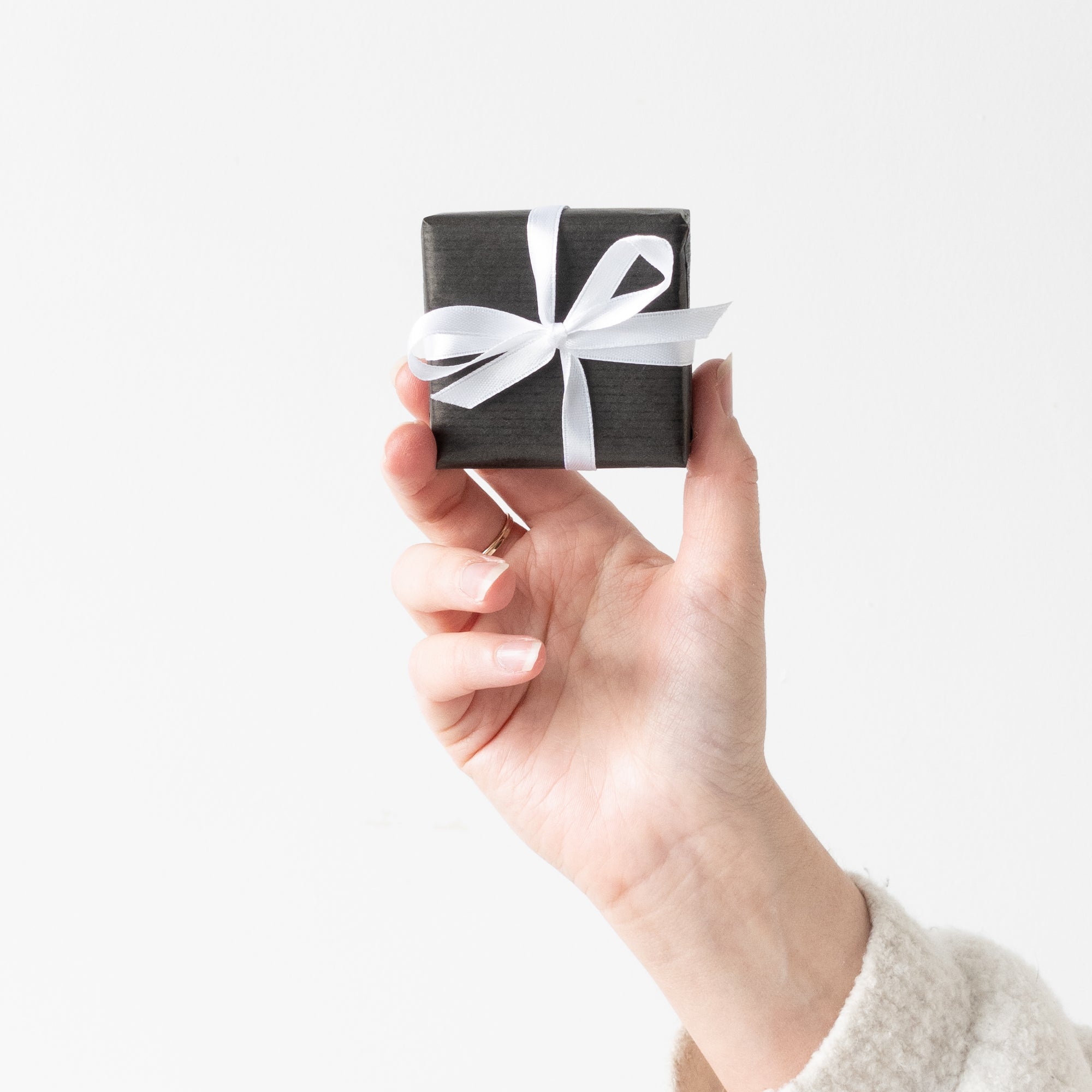 Hand holding a small black gift box with a white ribbon against a light background