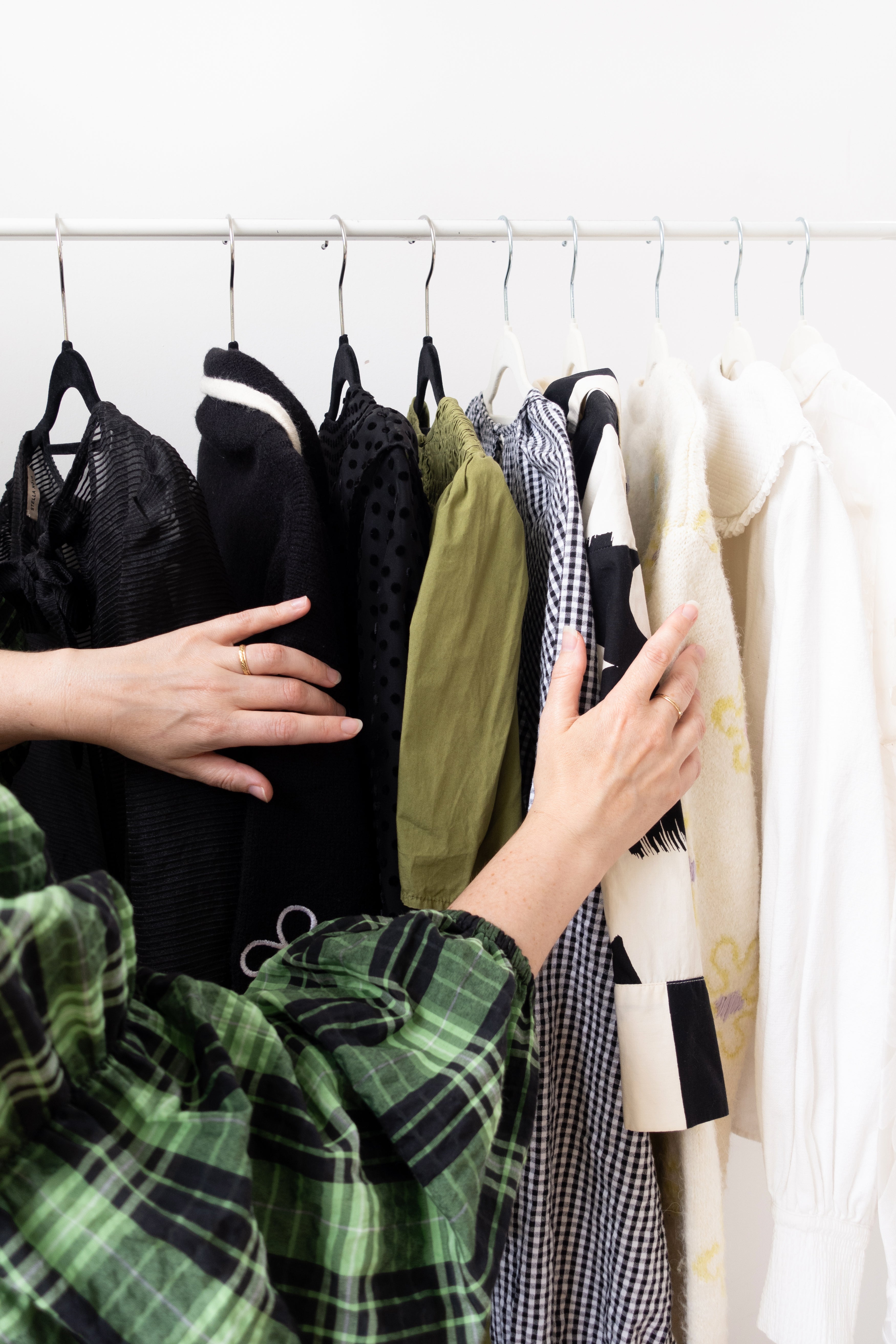 Person selecting clothes from a rack with various garments on hangers.
