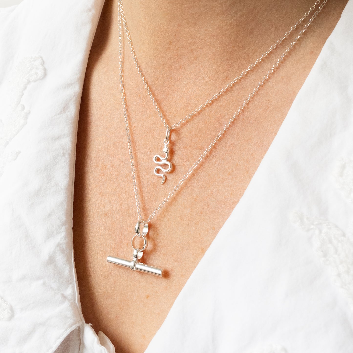 Silver necklaces with charms on a person wearing a white shirt