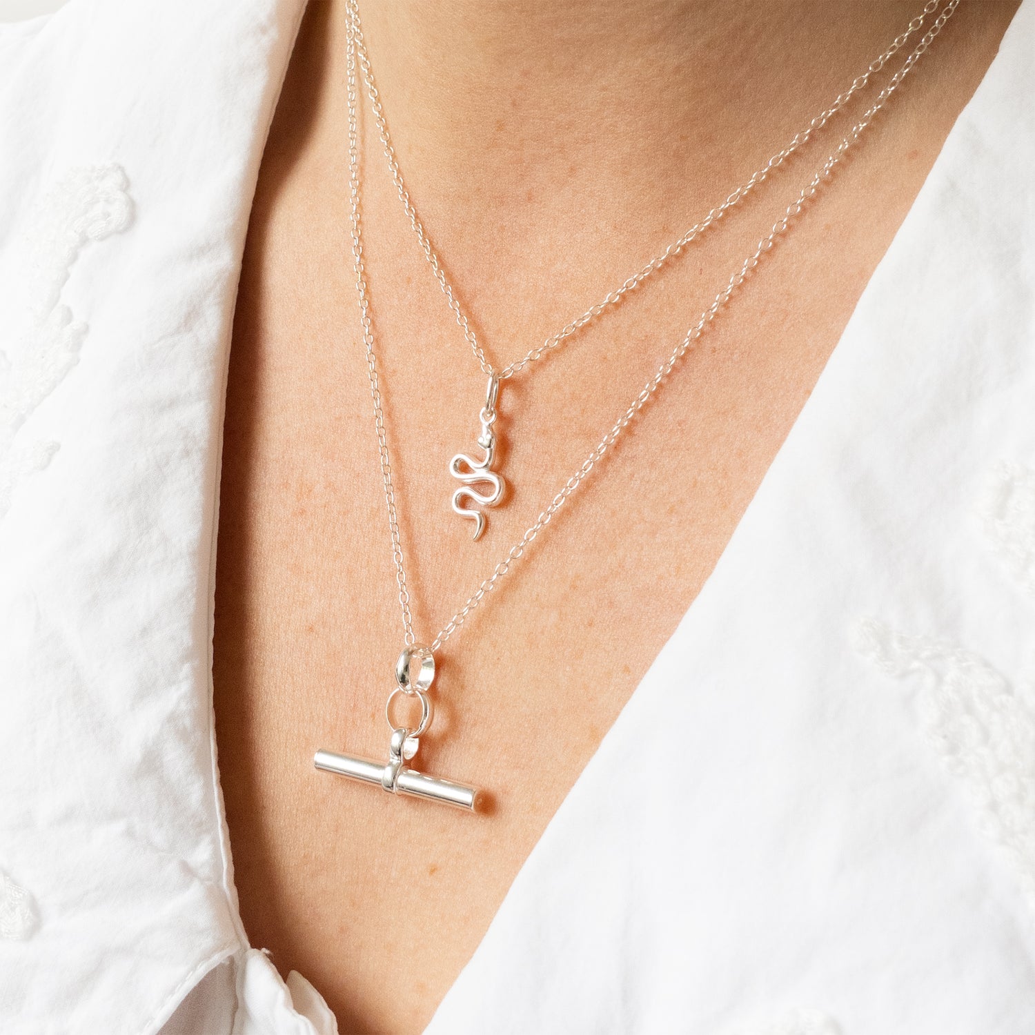 Silver necklaces with charms on a person wearing a white shirt