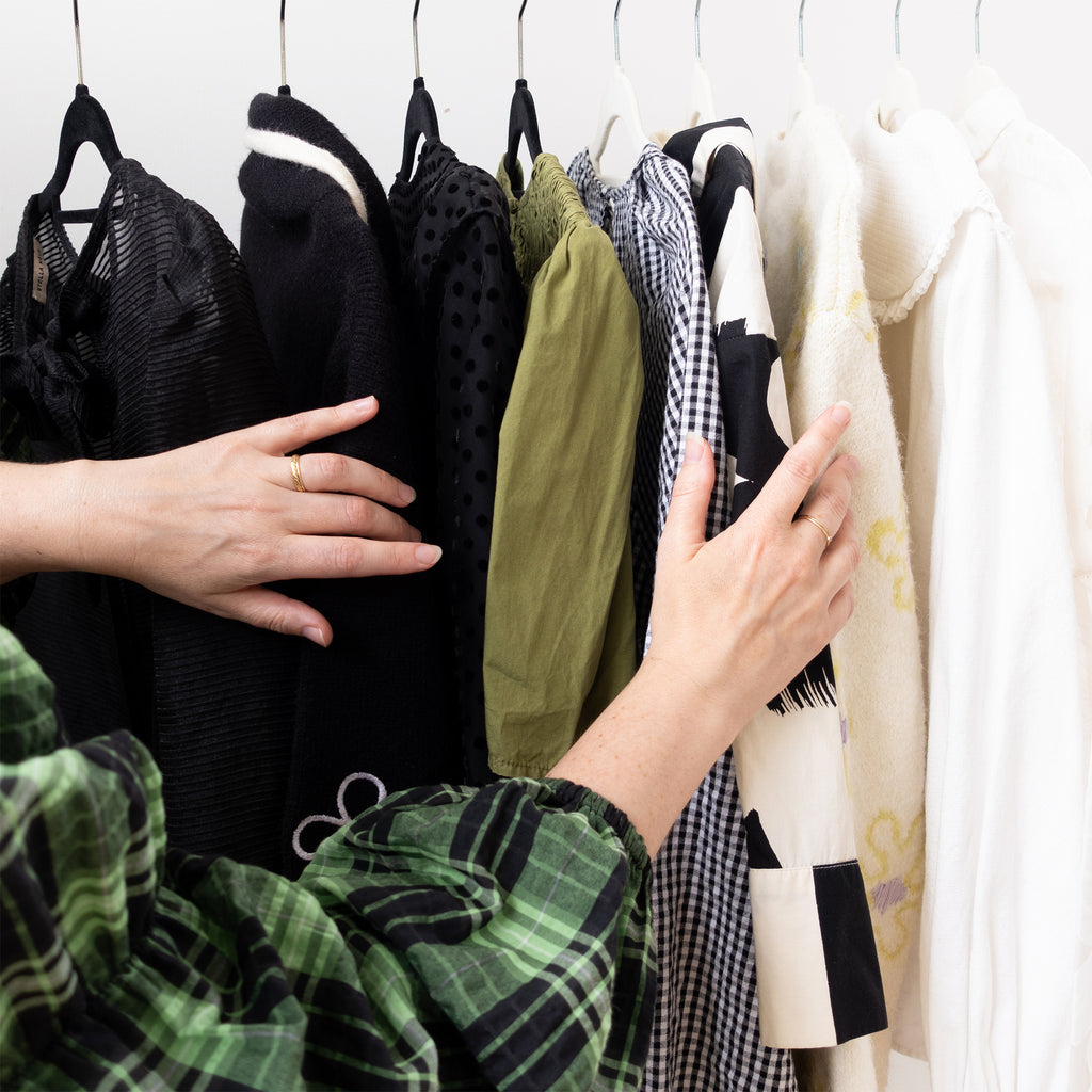 Person selecting clothes from a rack with various garments on hangers.