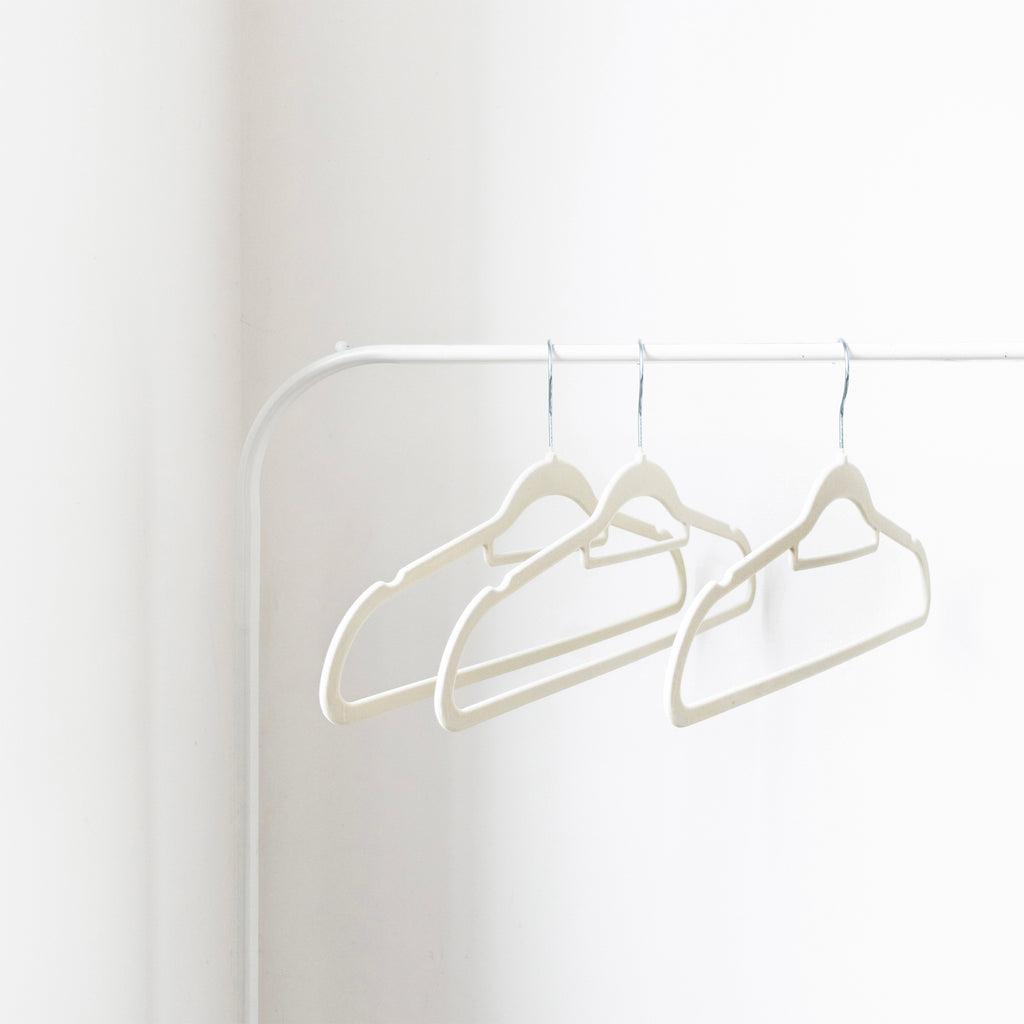 Three white hangers on a white rod against a white wall