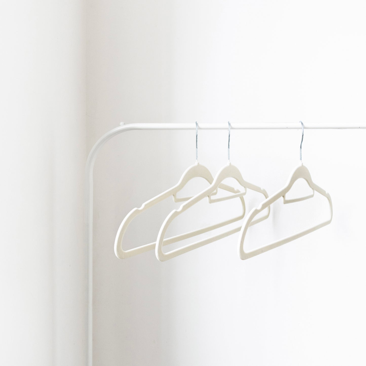 Three white hangers on a white rod against a white wall