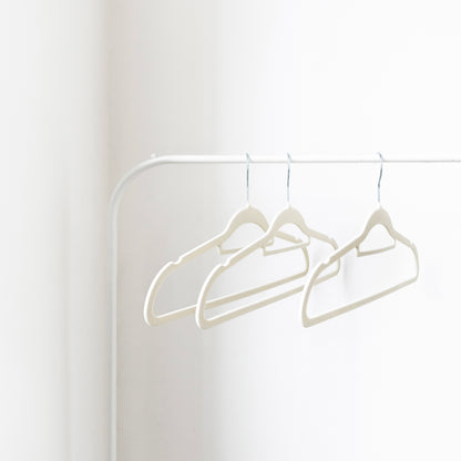 Three white hangers on a white rod against a white wall