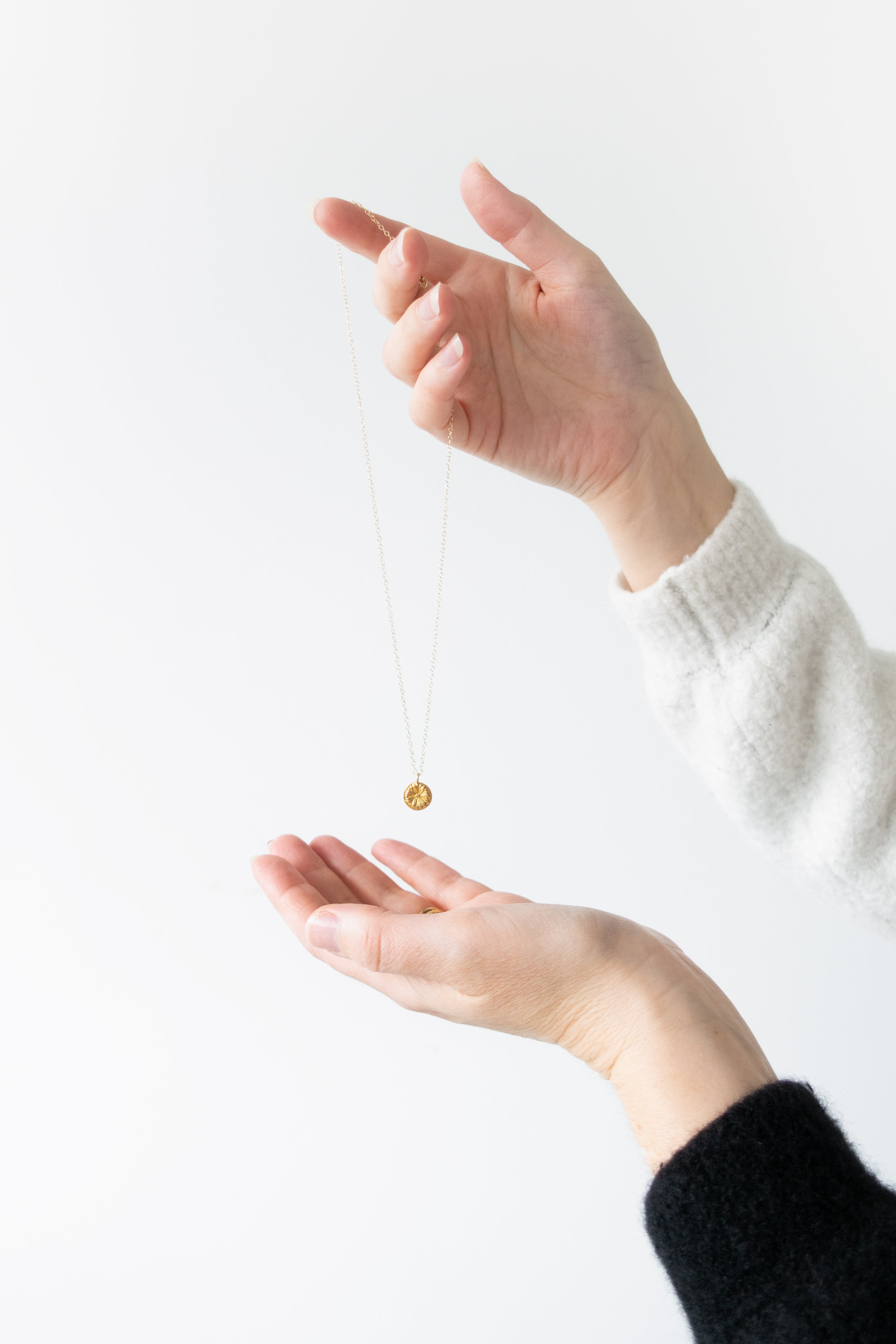 Hand holding a necklace above another hand against a white background