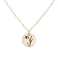 A gold birth flower necklace with an engraved pendant on a delicate cable chain, featuring a narcissus for the month of December.