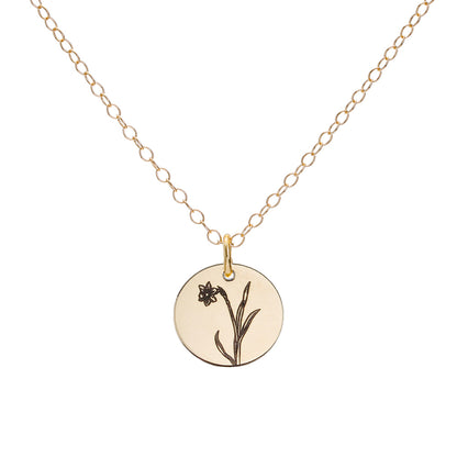 A gold birth flower necklace with an engraved pendant on a delicate cable chain, featuring a narcissus for the month of December.
