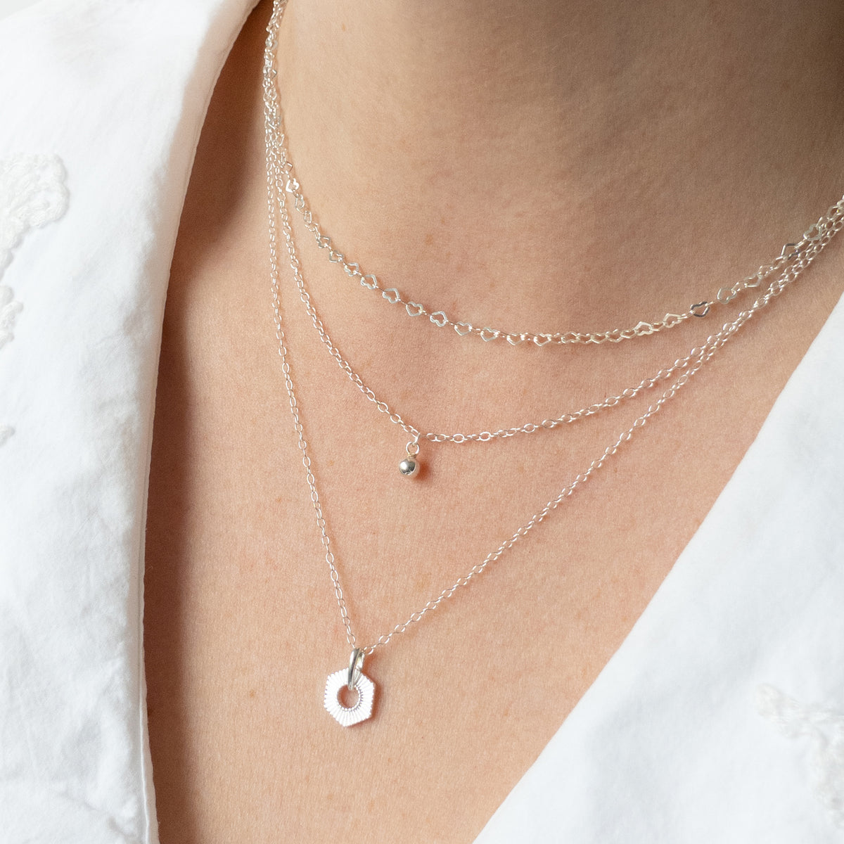 A close-up of a person's neck and chest wearing a layered silver necklace set with a geometric pendant.