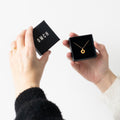 Person holding a gold necklace in a black box with 'OMCH' branding.