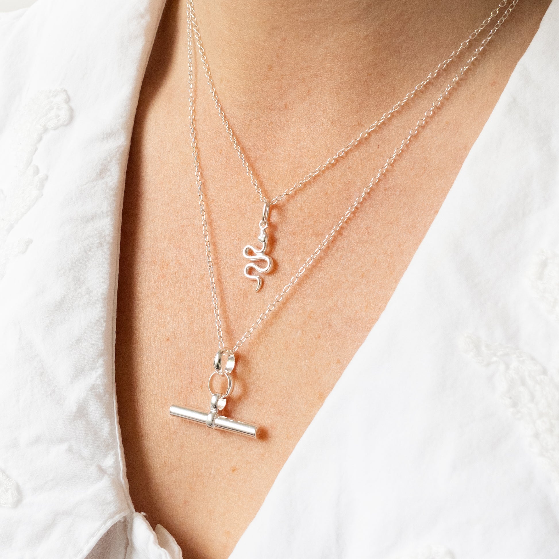 Silver necklaces with charms on a person wearing a white shirt