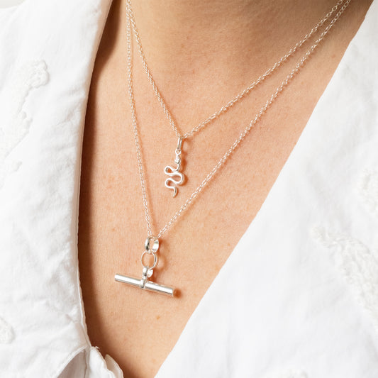 Silver necklaces with charms on a person wearing a white shirt